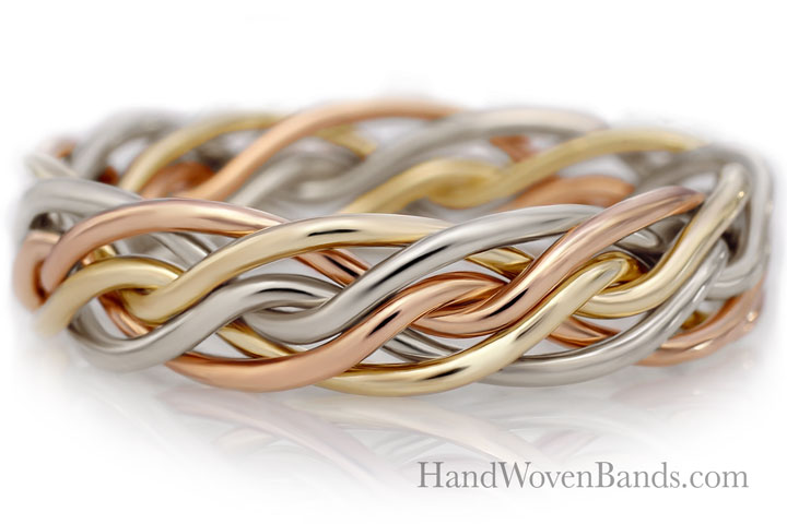 Close-up of a tri-color handwoven band made of intertwined yellow gold, silver, and rose gold strands, set against a reflective white surface.