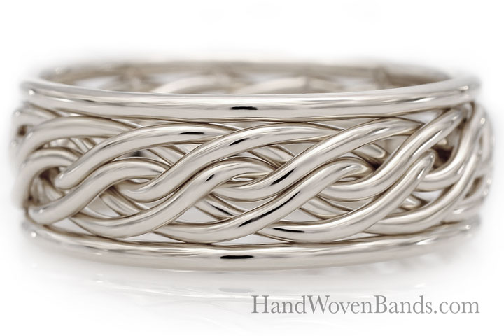 A white gold braided wedding band displayed on a reflective surface with the website "handwovenbands.com" labeled below.