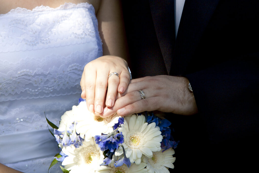 Close-up of a newlywed couple's hands over a bouquet, showcasing their wedding rings from the top wedding ring stores.