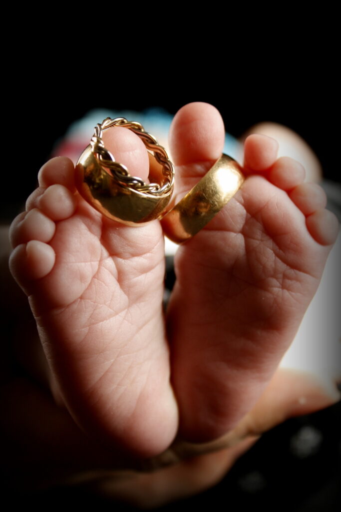 Close-up of a hand holding two interlocked gold wedding bands from wedding ring stores, with focus on the rings against a softly blurred dark background.