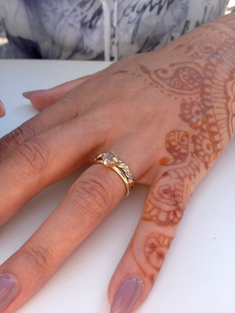 Close-up of a hand adorned with henna designs and wearing a wedding ring, resting on a white surface.