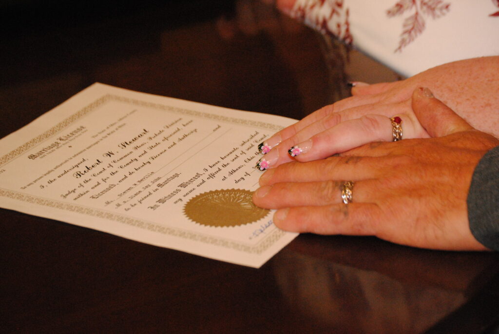 Two people holding hands over a marriage certificate on a wooden table, showcasing a moment of unity with visible wedding rings from wedding ring stores.