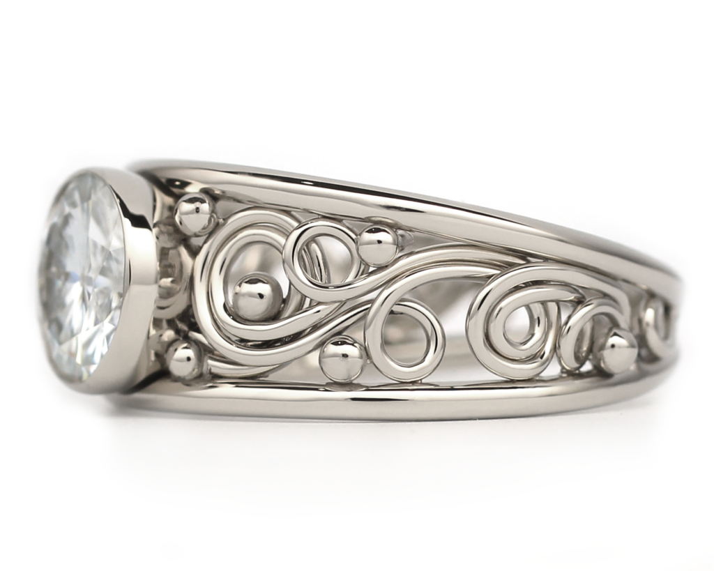 Silver ring featuring intricate filigree patterns with a prominent round diamond, uniquely designed as a Mother's Ring, set on a white background.