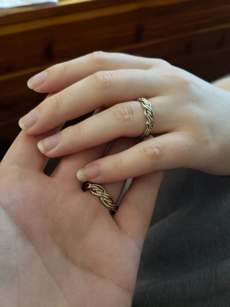 A close-up of two hands gently clasped together, each adorned with a five-strand gold ring.