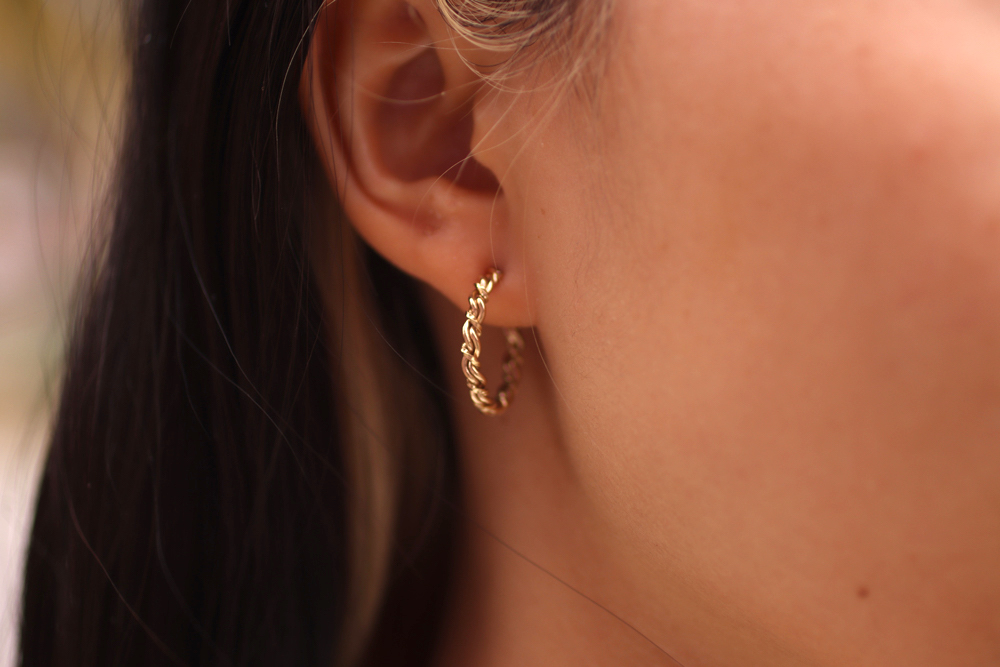 Close-up of a woman's ear wearing a small artistic gold hoop earring.