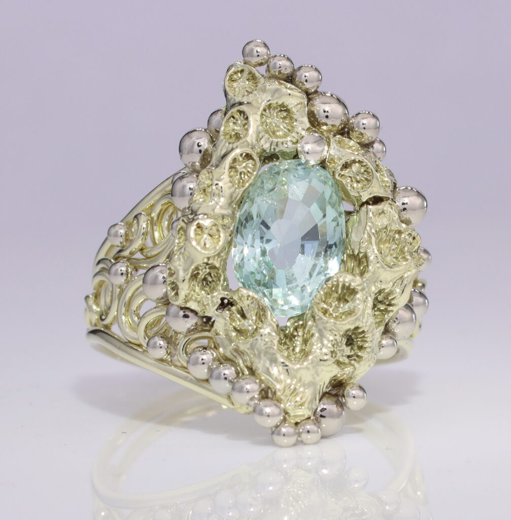 An ornate ring crafted for gold investing, featuring a large pale blue gemstone surrounded by intricate floral metalwork and small bead details.