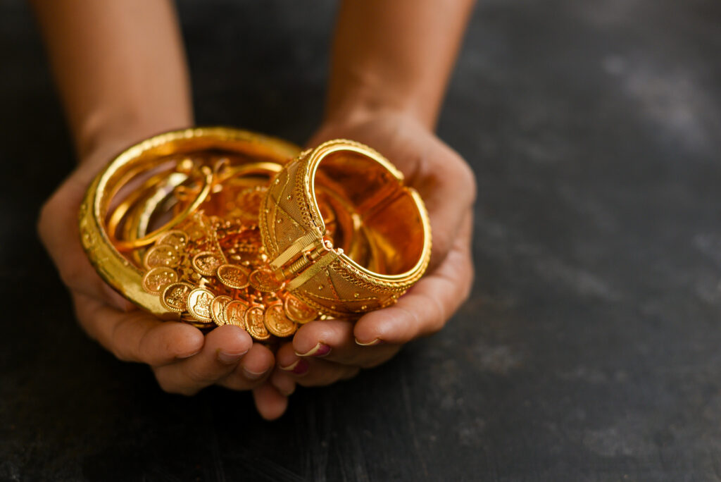 Hands holding a collection of gold investment bracelets and bangles against a dark background.