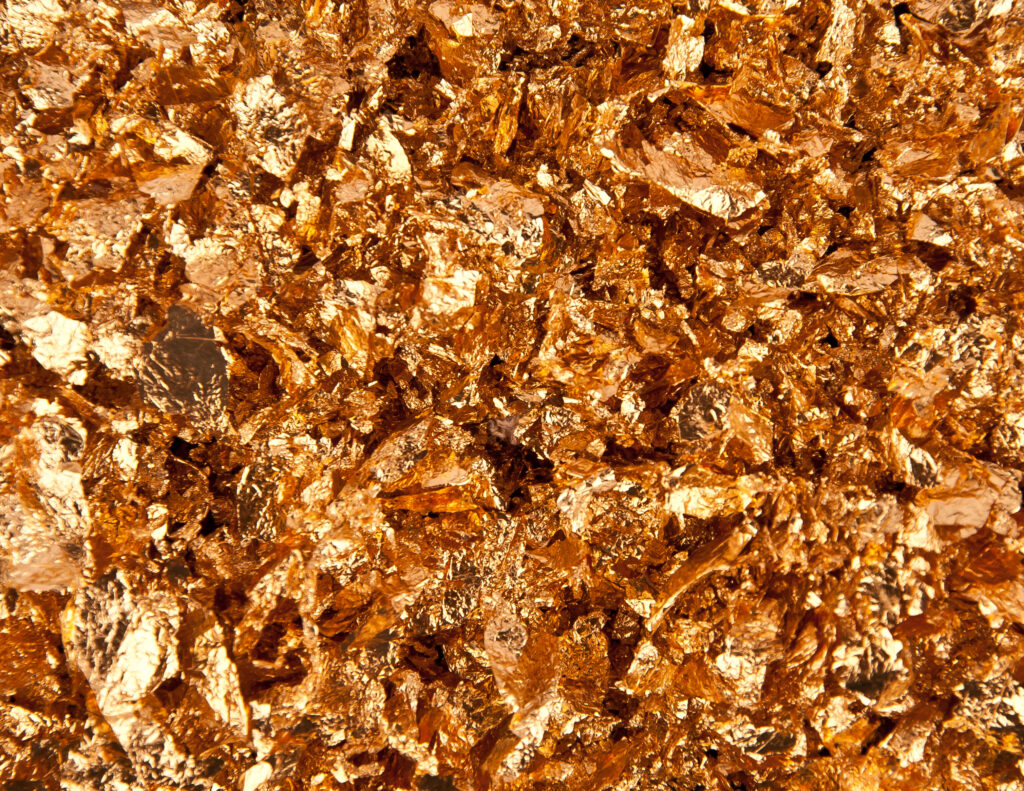 A close-up image of textured gold leaf flakes covering a surface, showing detailed, shiny, and crinkled pieces in the gold market.