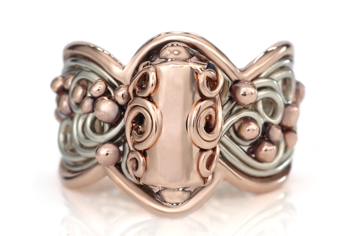 An intricately designed memorial jewelry piece featuring rose gold and silver tones with embossed bead patterns on a reflective white surface.