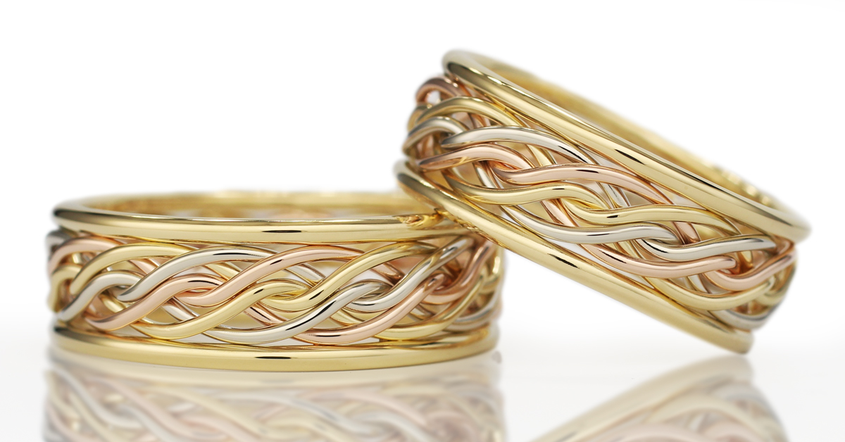 Two tri-color braided gold rings with an open weave design on a reflective surface with a white background.
