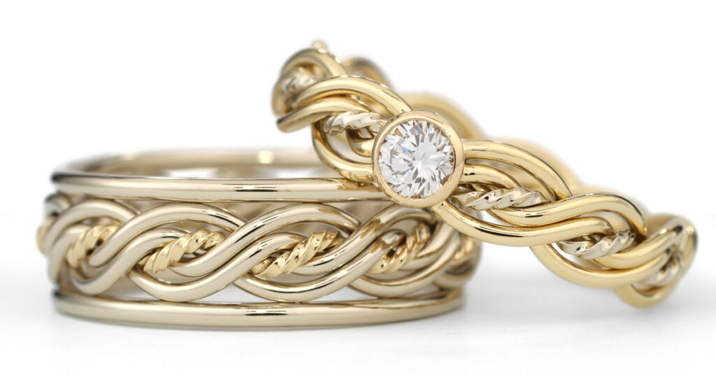 Two intertwined gold rings, one featuring a chain-link design and the other with a solitaire diamond, set against a white background. Alongside them rests a Five Strand Ring, enhancing the elegant display.