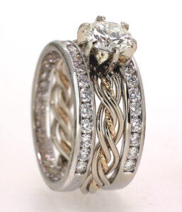 A close-up image of a diamond engagement ring paired with a wedding band, featuring intricate silver and gold twisted details and smaller embedded diamonds.