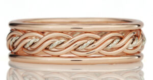 A detailed image of a ring with intertwined rose gold and silver bands, displayed against a reflective white surface.