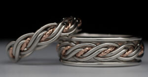 Two intertwined silver and rose gold bracelets on a black background, showcasing an elegant, twisted design.