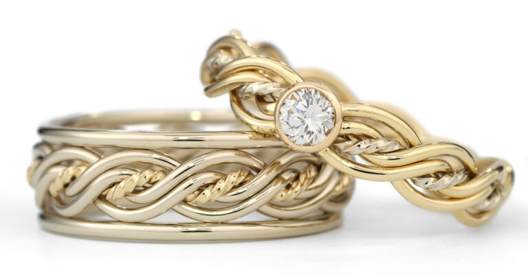 Five strand gold and silver intertwined band rings with a single diamond set in the gold ring, on a white background.