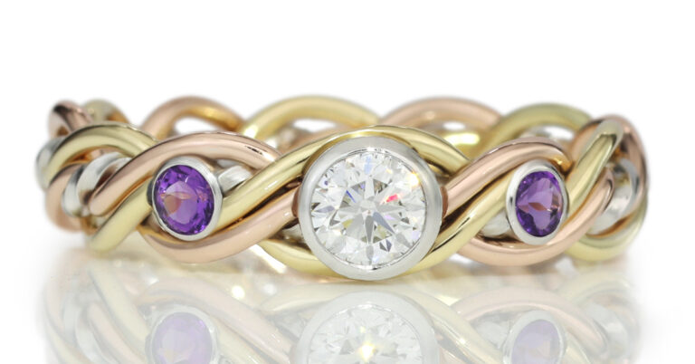 A tri-colored gold braided ring featuring a central large diamond and two smaller diamonds on a reflective surface.