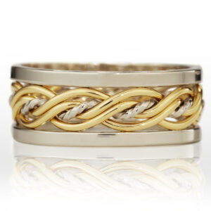 A two-toned metal ring featuring interlaced gold and silver bands, displayed on a reflective surface.