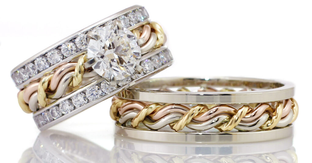 Two diamond-encrusted wedding rings, one with a large central stone and braided wedding bands, against a reflective white background.