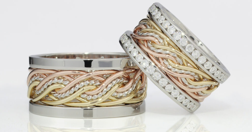 Two intertwined multicolored gold and diamond braided wedding rings against a reflective white background.