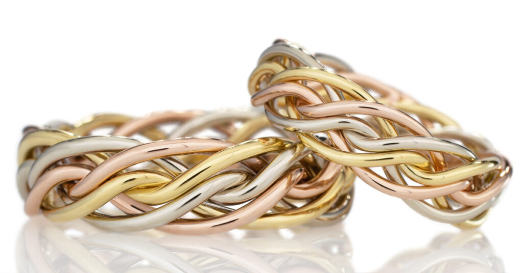 A close-up image of intertwined gold, silver, and rose gold braided wedding bands with a reflective surface.