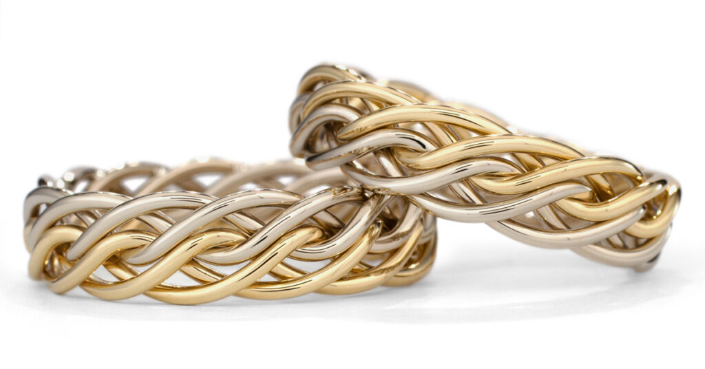 Two intertwined gold and silver bracelets with a thick, braided design, showcased against a white background.