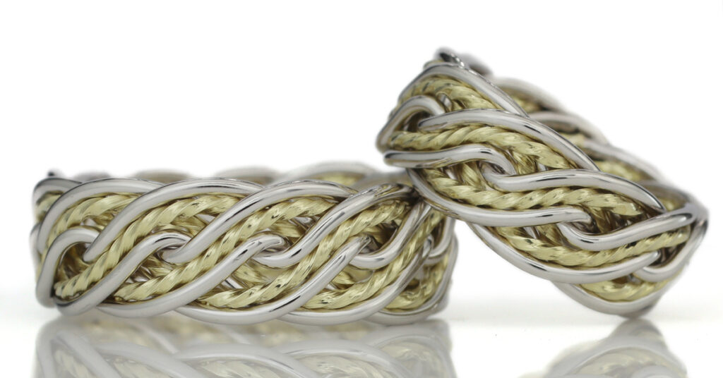 A close-up of braided wedding rings crafted from intertwined silver and gold threads, isolated against a white background.