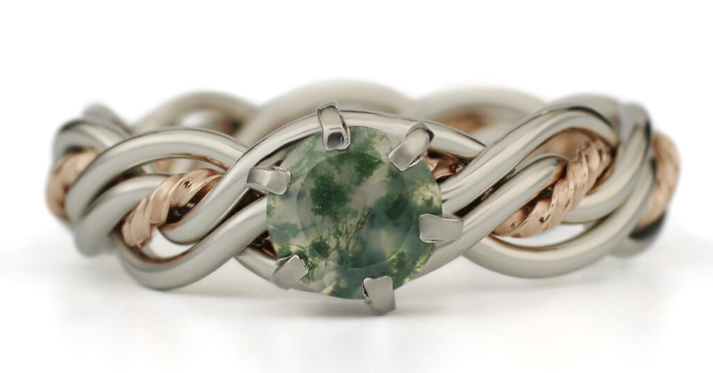 A silver and rose gold bracelet featuring a central large green gemstone and additional small gemstones held by metal prongs, against a white background.