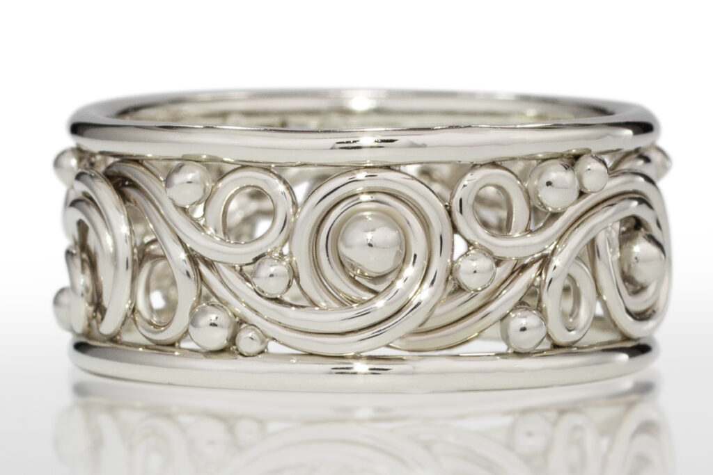Silver filigree ring with intricate braided patterns and bead details, displayed against a white background.