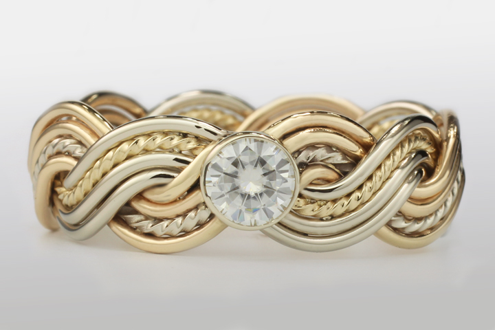 A gold eight-strand closed weave bracelet featuring a central large diamond on a reflective white surface.