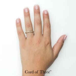 Gold braided ring with unique handwoven design on manicured hand. Cord of Three™ wedding ring by Todd Alan.