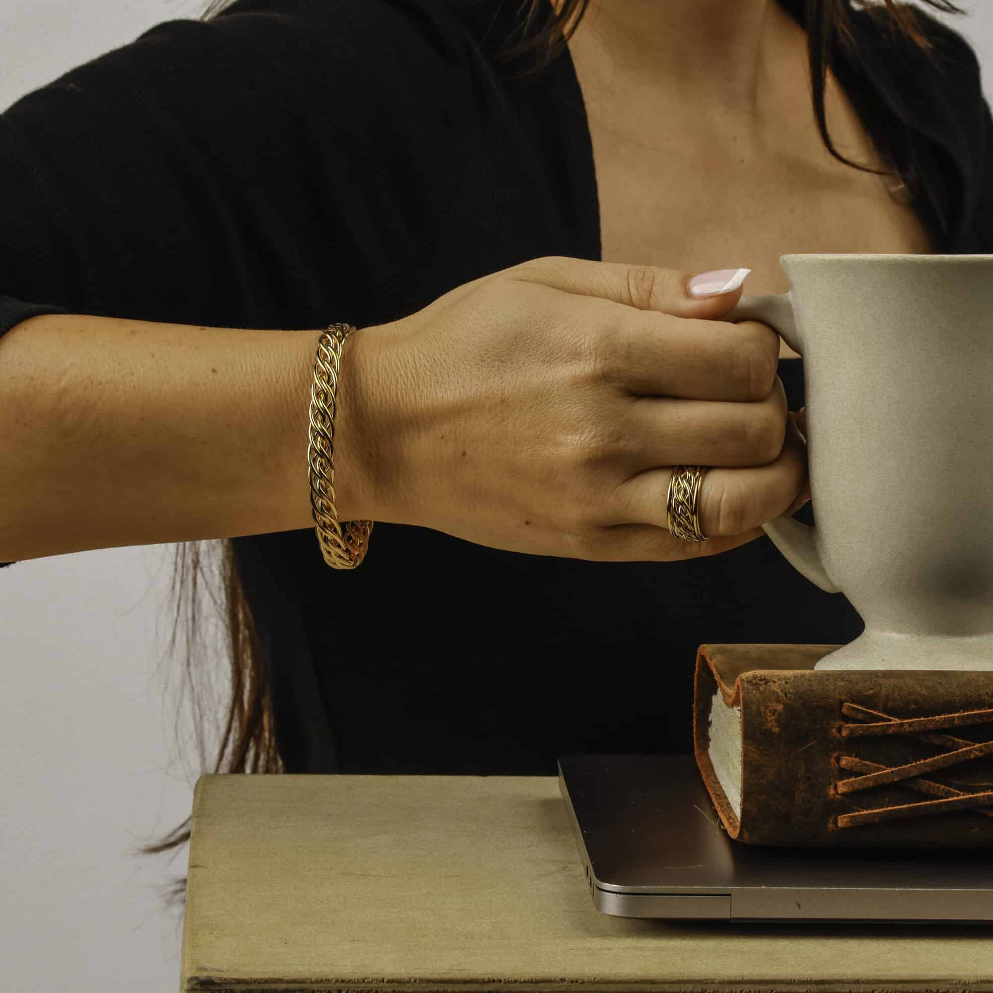 Handwoven gold braided ring with unique craftsmanship on hand holding mug; elegant style by Todd Alan.