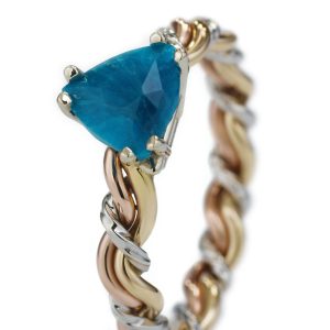 A close-up of a tricolor gold bracelet featuring multiple large, pear-shaped blue gemstones set in prong settings.